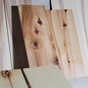 Op de afbeelding: Close-up van verschillende stukken hout met een natuurlijk houtnerfpatroon. Het hout heeft een lichtbruine kleur met donkerbruine knoesten en swirls. Het hout is glad en gepolijst.
