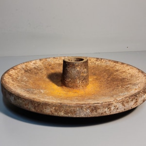 May include: A rusty metal disc with a raised center post. The disc is a light brown color with patches of yellow rust.