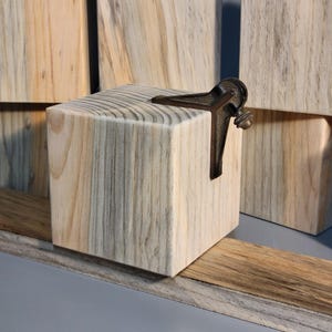 May include: A wooden block with a metal tool attached to it. The block is made of light wood with dark brown streaks. The tool is a metal protractor with a black handle.