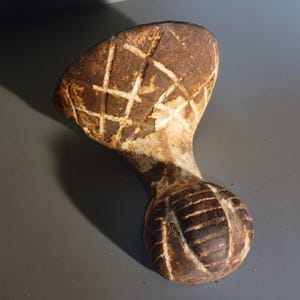 May include: A cast iron claw foot with a white and brown patina. The foot has a decorative design of intersecting lines and a round ball shape at the end.