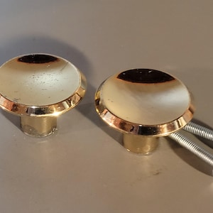 May include: Two gold-toned cabinet knobs with a rounded, slightly domed top and a smooth, shiny finish.