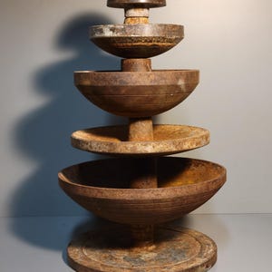 Puede incluir: Un soporte de metal oxidado de varios niveles con una parte superior redondeada y una cúpula marrón oscura. El soporte es de estilo rústico e industrial y sería perfecto para exhibir objetos pequeños.