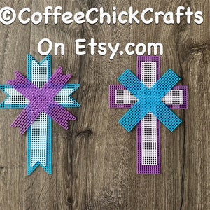 May include: Two white plastic crosses with purple and blue ribbon designs. The crosses are on a wood background.