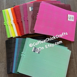 May include: A collection of rectangular plastic canvas sheets in a variety of vibrant colors including neon green, yellow, orange, red, magenta, maroon, black, blue, dark green, and light green, featuring a grid pattern and product labels.