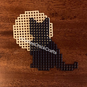 May include: Black cat silhouette on a beige canvas background. The cat is sitting with its tail curled around its body. The canvas is made of plastic mesh.