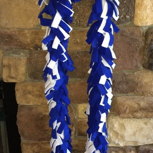 May include: A blue and white fleece dog toy with long, knotted strands. The toy is hanging from a hook on a stone wall.