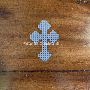 May include: A white plastic cross with a grid pattern. The cross is on a brown wooden surface. ©CoffeeCrickCrafts