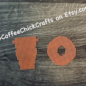 May include: Two orange plastic canvas shapes: a coffee cup and a donut. The coffee cup is a tall, tapered shape with a handle. The donut is a circle with a hole in the center. The background is a dark wood grain surface. Text in the image says "CoffeeChickCrafts on Etsy.com".