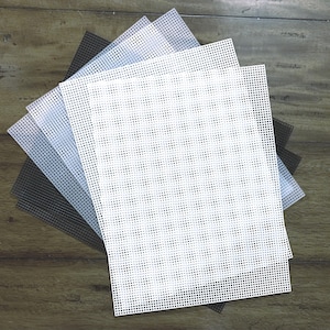 May include: A set of four plastic canvas sheets in black, white, gray, and light gray. The sheets are square and have a grid pattern.