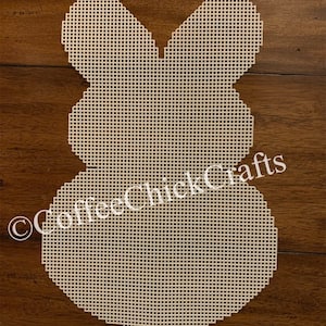 May include: A white plastic canvas shaped like a bunny rabbit. The canvas is blank and ready for embroidery. The canvas is on a wooden surface.