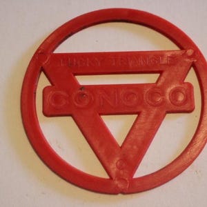 May include: A red plastic "Lucky Triangle" Conoco gas station promotional item. The design features a triangle within a circle, with the words "LUCKY TRIANGLE" and "CONOCO" in the center.