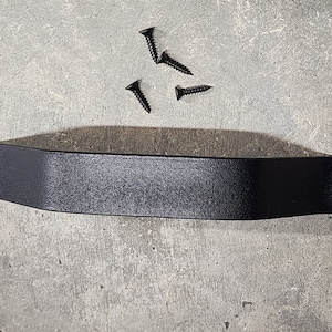 May include: A matte black metal cabinet handle with a textured finish and a slightly arched center. The handle features two circular mounting holes on each end. Four matching black metal screws are included for installation purposes.