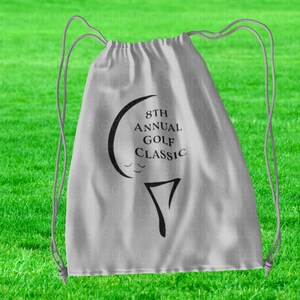 May include: A white drawstring bag with a black golf ball and tee design. The text "8th Annual Golf Classic" is printed on the bag.