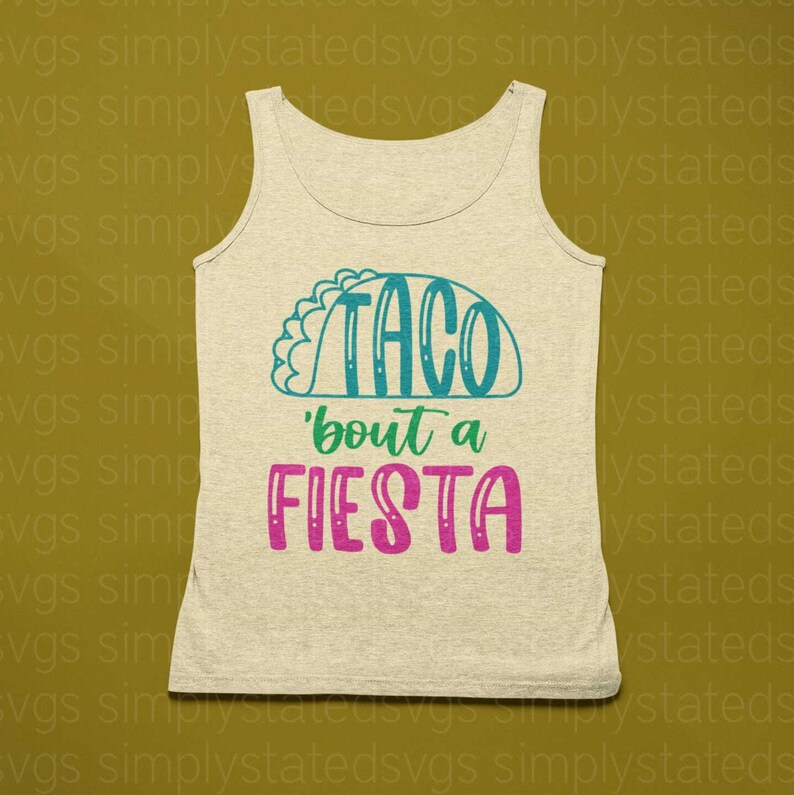 May include: A beige tank top with the text "Taco 'bout a Fiesta" in teal and pink lettering. The text is stylized to look like a taco.