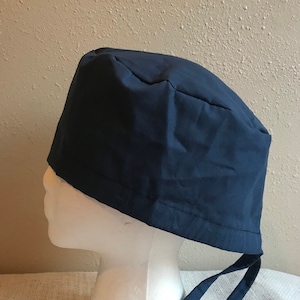 May include: A dark blue scrub hat with a tie. The hat is made of a soft, comfortable fabric and is designed to be worn by medical professionals.
