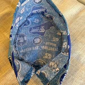 May include: A light blue and white patterned fabric hat featuring the words "North Carolina" and the university logo. The hat is made of fabric and has a black stitched seam.