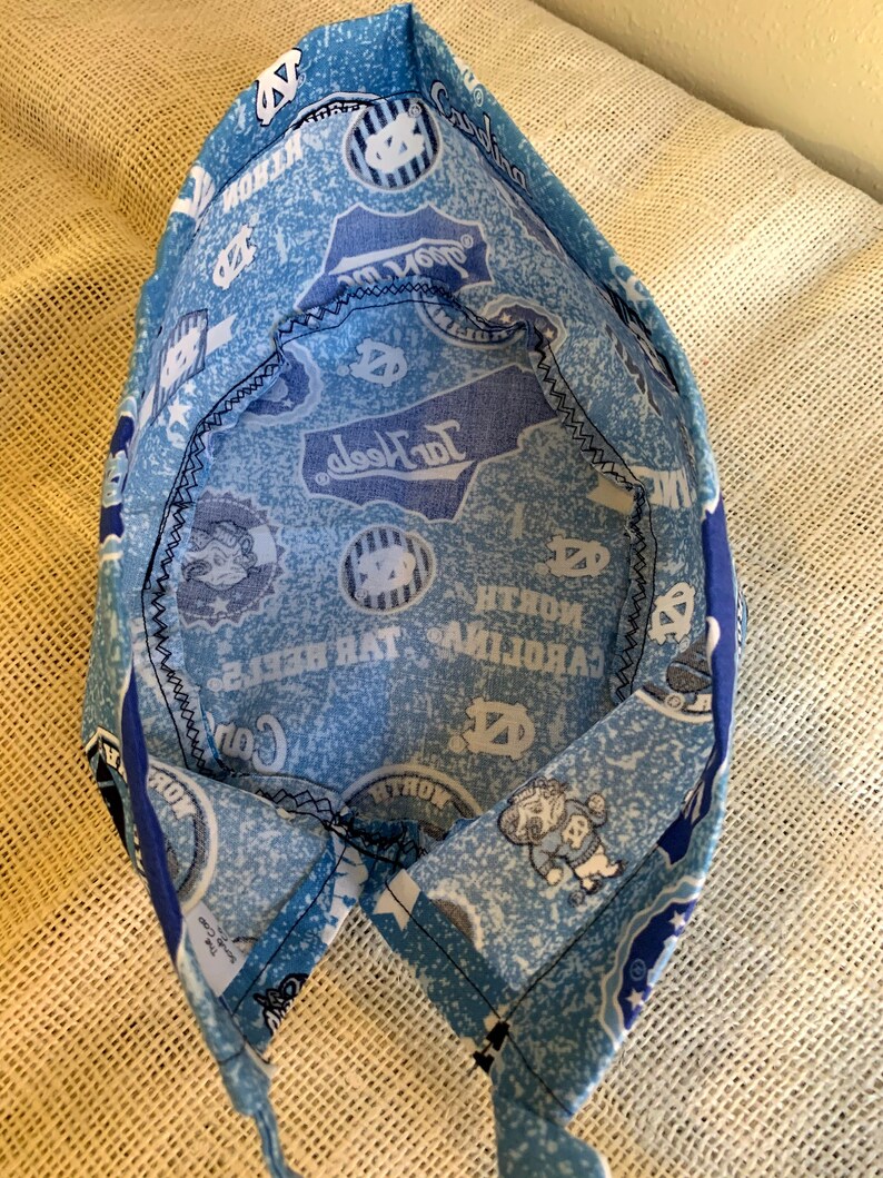 May include: A light blue and white patterned fabric hat featuring the words "North Carolina" and the university logo. The hat is made of fabric and has a black stitched seam.