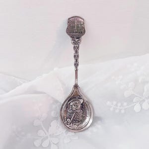 May include: Silver souvenir spoon with an ornate handle and a depiction of a man with a beard and a pipe on the bowl. The handle features a design of a building with the word "Innsbruck" on it.