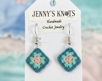 Könnte beinhalten: Handgefertigte Häkelohrringe. Jeder Ohrring hat ein quadratisches Design mit einem türkisfarbenen Rand und einem rosa-türkisfarbenen Blumenzentrum. Die Ohrringe werden auf einer weißen Karte mit dem Text "JENNY'S KNOTS Handmade Crochet Jewelry" präsentiert.