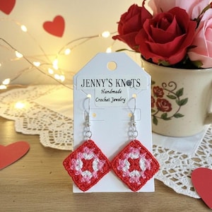 May include: Handmade crochet earrings in a square design with red, white, and pink colors. The earrings are displayed on a white card with the text "JENNY'S KNOTS Handmade Crochet Jewelry". The background includes red heart cutouts and a vase of roses.