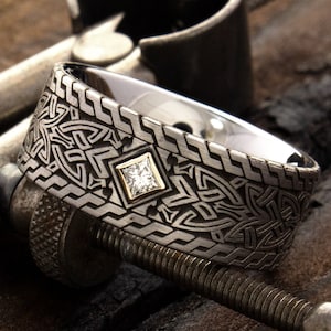 Puede incluir: Un anillo de plata con un diseño de nudo celta y un pequeño diamante en el centro. El anillo está sobre una superficie de madera.