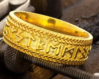 May include: A gold ring with a braided band and runes engraved around the band.