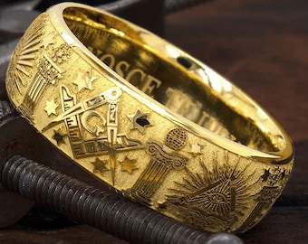 May include: A gold Masonic ring with intricate engravings of symbols and text, including a compass, square, and the all-seeing eye. The ring is set against a wooden background.