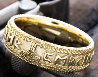 May include: A gold band ring with a braided design and a raised inscription in Old Norse runes. The inscription reads "HAMR EMBR", which translates to "Hammer of the Embla".