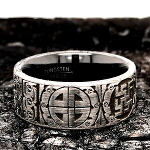 Peut inclure: Une bague en carbure de tungst&egrave;ne argent&eacute;e avec une bande noire et un motif complexe en forme de cercle &agrave; quatre points. La bague est grav&eacute;e des mots "Tungsten Carbide".