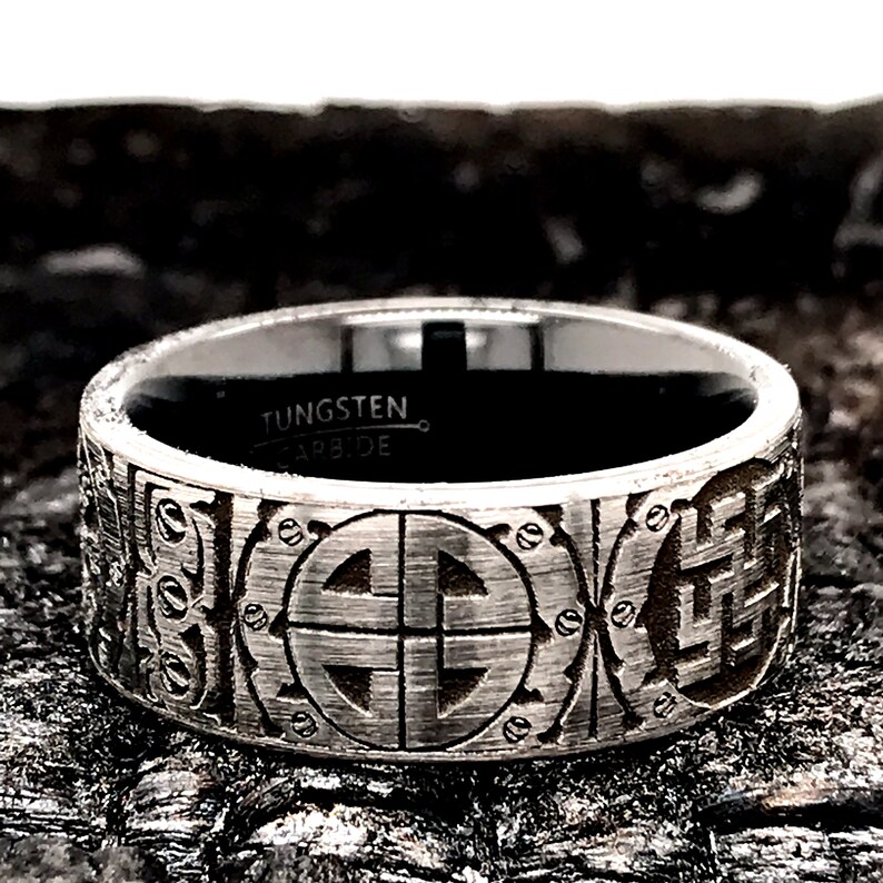 Peut inclure: Une bague en carbure de tungst&egrave;ne argent&eacute;e avec une bande noire et un motif complexe en forme de cercle &agrave; quatre points. La bague est grav&eacute;e des mots "Tungsten Carbide".