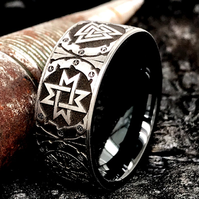 Peut inclure: Une bague noire et argent&eacute;e avec des gravures complexes de symboles nordiques, notamment le Vegvisir et le Mjolnir. La bague est en acier inoxydable et a une finition polie.