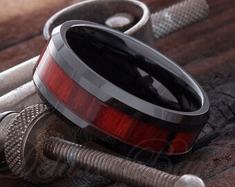 Op de afbeelding: Een zwarte ring van wolfraamcarbide met een rode houten inlay. De ring heeft een afgeschuinde rand en een gepolijste afwerking.