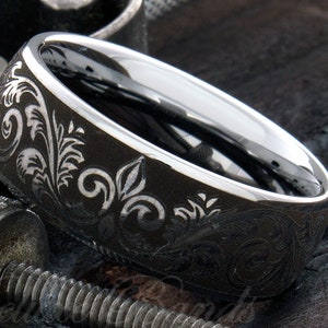 Puede incluir: Un anillo de metal gris oscuro con un interior plateado pulido y una superficie exterior mate grabada con un detallado patr&oacute;n de volutas florales. La banda tiene un perfil ancho con un borde liso y redondeado y un acabado met&aacute;lico.