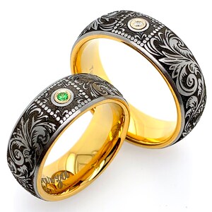 Puede incluir: Dos alianzas con intrincados grabados florales. Una alianza es de oro con una piedra transparente, la otra es negra con una piedra verde.