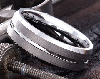 May include: A silver tungsten carbide ring with a bevelled edge and a brushed finish. The ring has a single, thin, polished groove around the centre.
