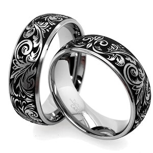 Puede incluir: Dos anillos de tono plateado con una incrustaci&oacute;n negra y un intrincado patr&oacute;n floral grabado. El interior de los anillos es de plata pulida e incluye el texto Tungsten Carbide grabado en la superficie interior de la banda.