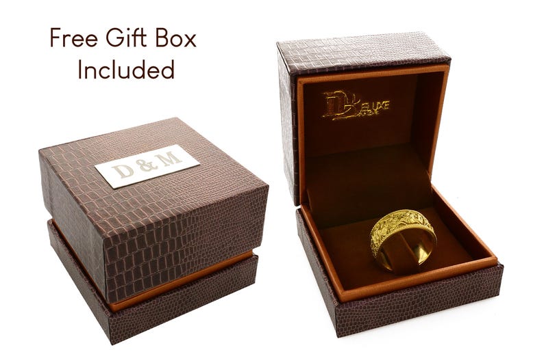 Puede incluir: Un anillo dorado con un patr&oacute;n texturizado intrincado se encuentra dentro de un joyero marr&oacute;n con relieve de cocodrilo. La tapa presenta una placa rectangular plateada con el texto D & M, mientras que el interior muestra el texto Deluxe.