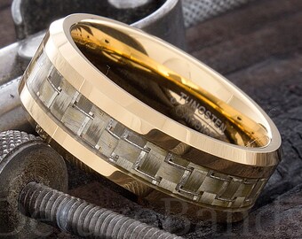 May include: A gold tungsten carbide ring with a black and white carbon fiber inlay. The ring is beveled and has a polished finish.