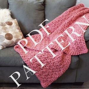 May include: A pink crocheted blanket with a white "PDF PATTERN" text overlay. The blanket is draped over a grey sofa with a white and brown patterned cushion.