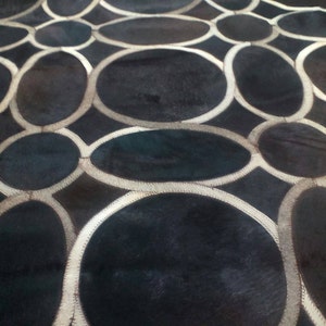 May include: Black and white patterned rug with a circular design. The rug is made of leather and has a soft, textured surface.