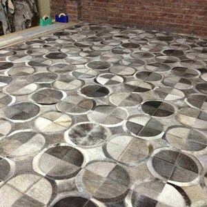 May include: A gray and white patterned rug made of cowhide. The rug has a geometric design with circles and squares.