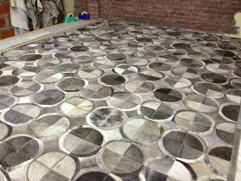 May include: A gray and white patterned rug made of cowhide. The rug has a geometric design with circles and squares.