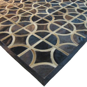 May include: A geometric patterned rug made of cowhide with a black border. The rug features a repeating pattern of circles and squares in shades of brown, beige, and black.