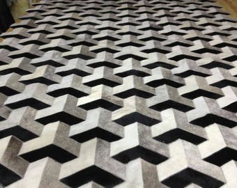 May include: A large, geometric patterned rug with a repeating 3D arrow design. The rug features a combination of black, white, and gray tones, creating a striking visual effect. The rug's texture appears soft and inviting, suitable for a living room or bedroom.
