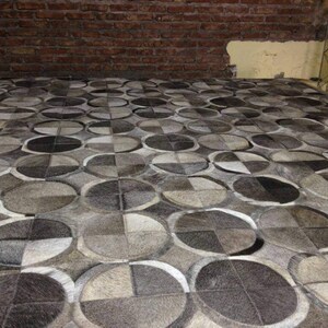 May include: A gray and white patterned rug made of cowhide. The rug is made up of many circles of different sizes.