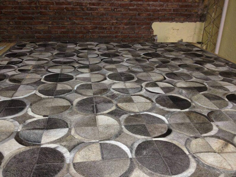 May include: A gray and white patterned rug made of cowhide. The rug is made up of many circles of different sizes.