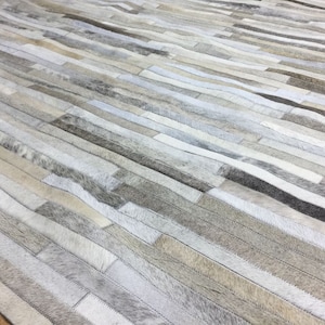 May include: A grey and white patchwork rug made of leather strips. The rug is made of different shades of grey and white leather strips sewn together to create a unique and stylish design.