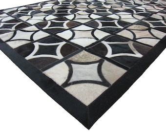 Può includere: Un tappeto geometrico in bianco e nero realizzato in pelle di mucca. Il tappeto ha un bordo nero ed è composto da quadrati e cerchi.