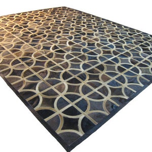 May include: A geometric patterned rug made of leather in shades of brown, black, and white. The rug has a dark brown border.