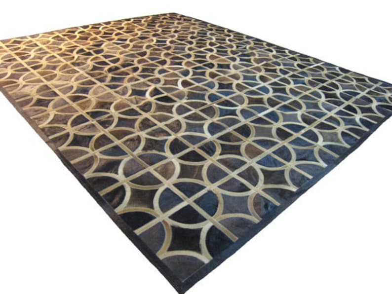 May include: A geometric patterned rug made of leather in shades of brown, black, and white. The rug has a dark brown border.
